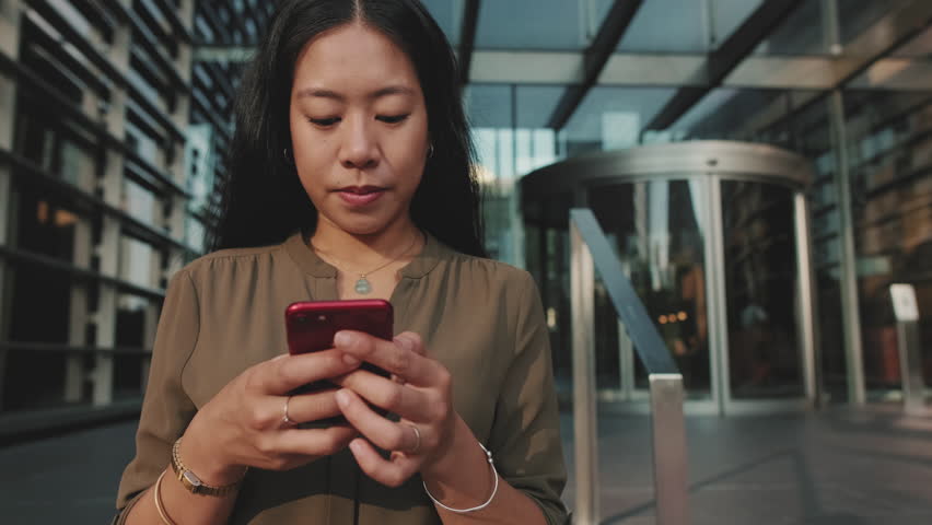 Young businesswoman using mobile phone while standing on business center background | Shutterstock HD Video #1099619373