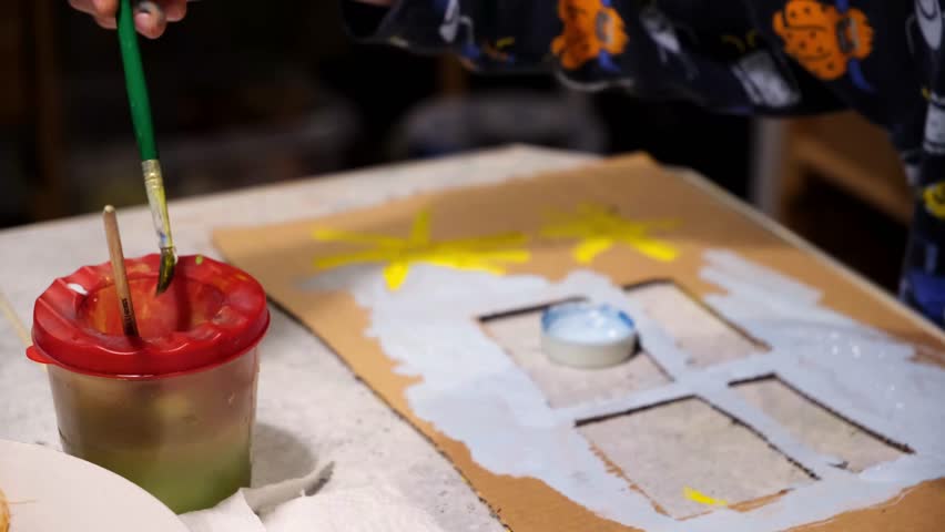 A little child wash painbrush in water glass. Brush in hand. Drawing of sun house with colored gouache paints on cardboard. Creative and Artistic hobby. Happy future concept. Kid dreams. Handicraft. | Shutterstock HD Video #1099620239