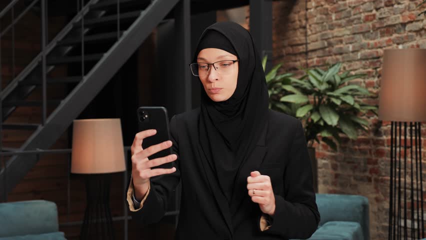 Cute beautiful young arabic businesswoman using modern smartphone, passing online job interview, distant communication. Confident business woman talk to webcam make video conference call in office.