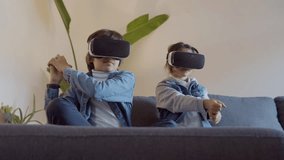 Happy boy and girl sitting on sofa and playing game in VR glasses. Children making fighting gestures, then taking off headsets and giving high five. Entertainment, modern technology concept - Powered by Shutterstock - Get 15% off with code: PIKWIZARD15