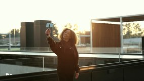 Woman recording content for her social networks with a mobile phone and a microphone while walking down the street. african american video blogger at sunset.