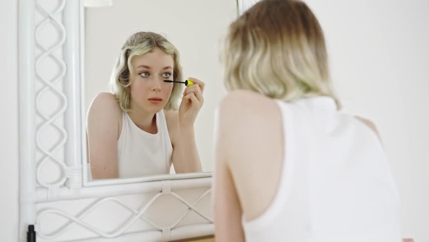 Teenage girl applying black mascara on lashes.