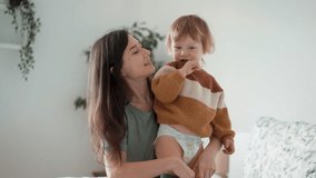 Young loving mother dresses beautiful infant boy kid, caring parent putting on sweater, do morning routine on baby toddler bright bedroom. Care, fashion comfort clothes, parenthood, cherish, babyhood - Powered by Shutterstock - Get 15% off with code: PIKWIZARD15