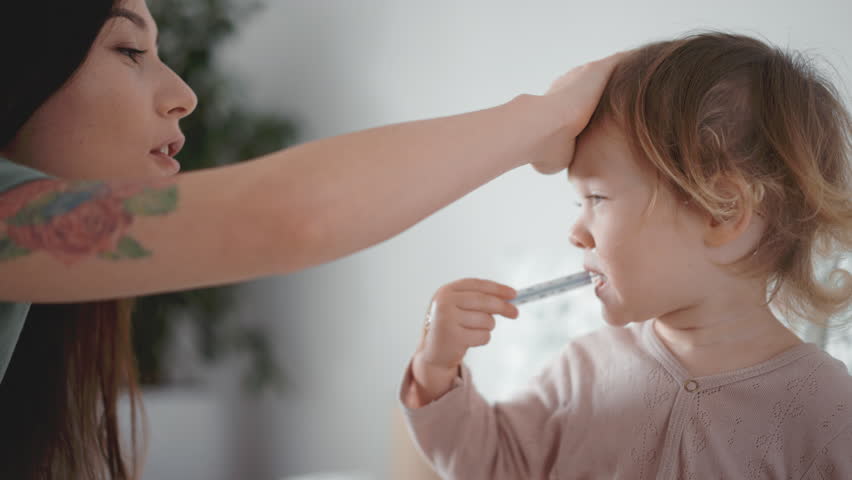 Pretty asian woman measure temperature of little girl or boy. Cute curly toddler sick at home in bedroom. Smiling kid put a thermometer at mouth. Home quarantine coronavirus. Closeup Influenza concept | Shutterstock HD Video #1099628401