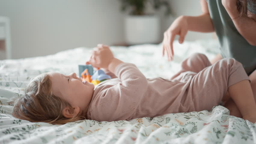 Happy carefree asian mother and cute small child boy tickling laughing having fun lying on sofa and playing, smiling mum enjoying bonding cuddling hugging spending time with little funny kid at home