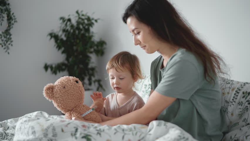 Pretty asian woman measure temperature of little girl or boy. Cute curly toddler sick at home in bedroom. Hugging teddy bear toy. Home quarantine coronavirus. Close-up. Influenza, cough, fever concept | Shutterstock HD Video #1099628409