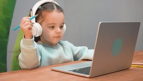A little girl with headphones studying online on a laptop, distance education.