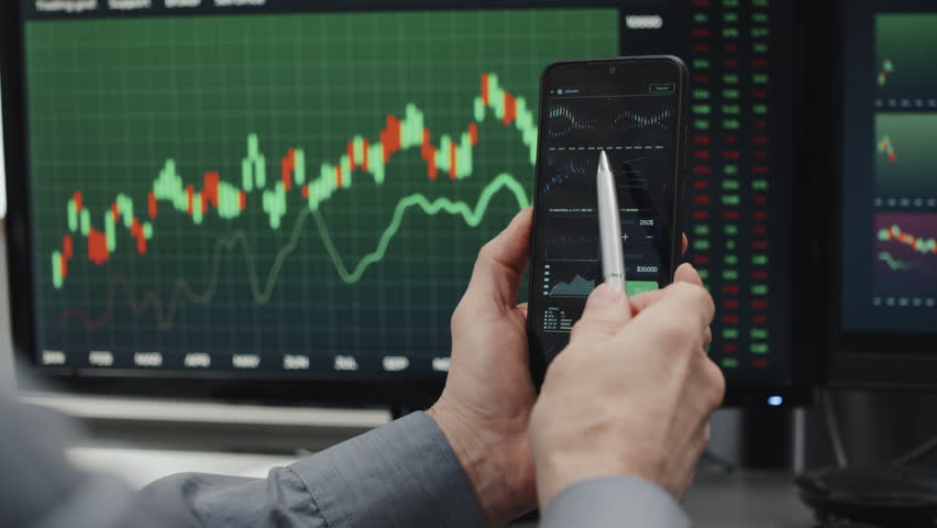 Unrecognizable mature brokerage company specialist sitting at desk with computer monitors on it holding smartphone working with data charts Royalty-Free Stock Footage #1099632633