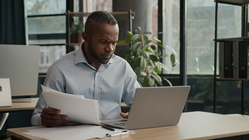 Tired exhausted African middle-aged office manager bookkeeper businessman American mature ethnic man read loan papers documents search mistake use computer business debt problem feel headache stress Royalty-Free Stock Footage #1099633875