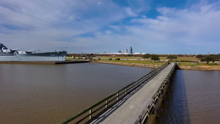 aerial footage of a long brown wooden pier over Mobile Bay with a man fishing at the end of the pier at sunrise with blue sky in Mobile Alabama USA