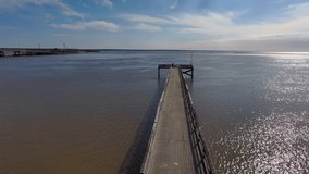 aerial footage of a long brown wooden pier over Mobile Bay with a man fishing at the end of the pier at sunrise with blue sky in Mobile Alabama USA