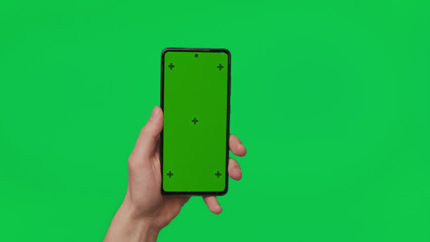 Male hand holding a smartphone with vertical green chroma key screen isolated on green. Mobile phone in a hand. Different signs and gestures with fingers. The concept of technology and internet. Royalty-Free Stock Footage #1099639733
