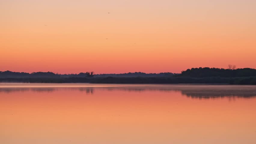 Early morning on calm river with fog. Sunrise over lake and beautiful morning landscape. Morning sun breaks through the thick fog. Fantastic foggy river in the golden sunlight on water surface