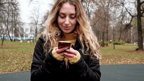 A beautiful woman reads a text from her phone standing in the park. High quality FullHD footage