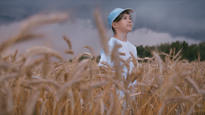 funny boy in a hat stands in a field at the beginning of a thunderstorm, looks at the rainy sky, cinematic steadicam shot