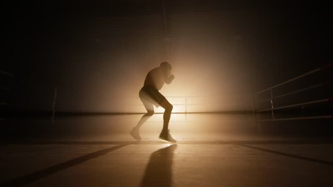 Close-up view of unrecognized, young boxer training indoors. Silhouette of a kickboxer having an intensive workout in the gym. High quality 4k footage in golden orange bronze foggy back light 스톡 비디오