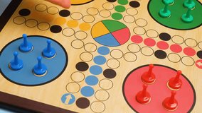 People play Ludo or Pachisi board game on beautiful wooden play board. Ludo is a strategy board game for two to four players. 4K resolution family board game video.