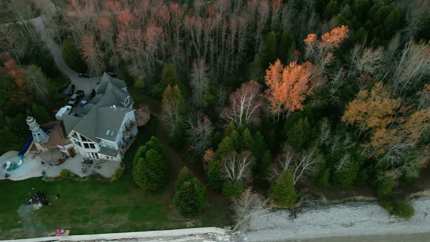 sliding aerial transforming into a orbiting shot of a large blue mansion with a private lighthouse sorounded by green trees in Wisconsin, USA
