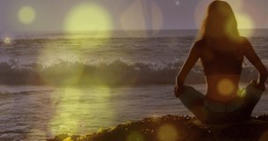 Animation of lights over back view of caucasian woman practicing yoga on beach. Active lifestyle, sport, relax and sea concept digitally generated video.