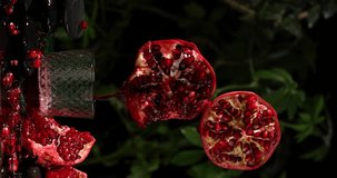 Vertical video of flying ripe pomegranate and pouring juice in glass and fresh fruits on against black background with green leaves, space for text, healthy drink concept, Levitation fruit
