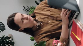 Vertical video of exhausted young woman massaging shoulder, suffering from pain, working typing on laptop at home office. Sad unhappy caucasian female freelancer touching aching neck. Business concept