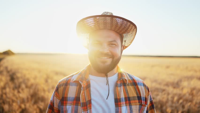 Portrait young adult caucasian man farmer in straw hat stands in rural wheat field in outdoors nature and looks at camera. Work in agriculture. Summer sun rays, season crop and rich golden harvest. | Shutterstock HD Video #1099663919
