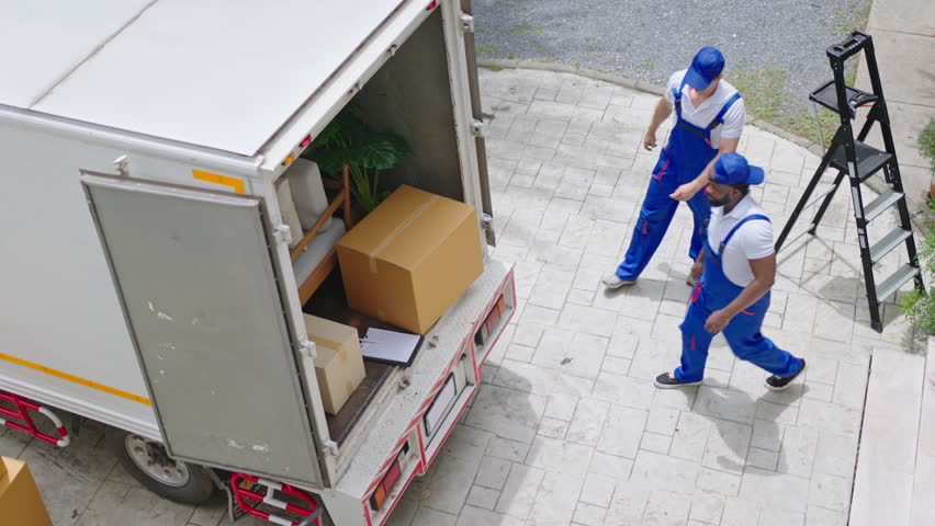 top view of Workers unloading boxes from van outdoors.House move, mover service and Moving service concept.Two young handsome worker wearing uniforms are unloading the van full of boxes.4k UHD video Royalty-Free Stock Footage #1099664195