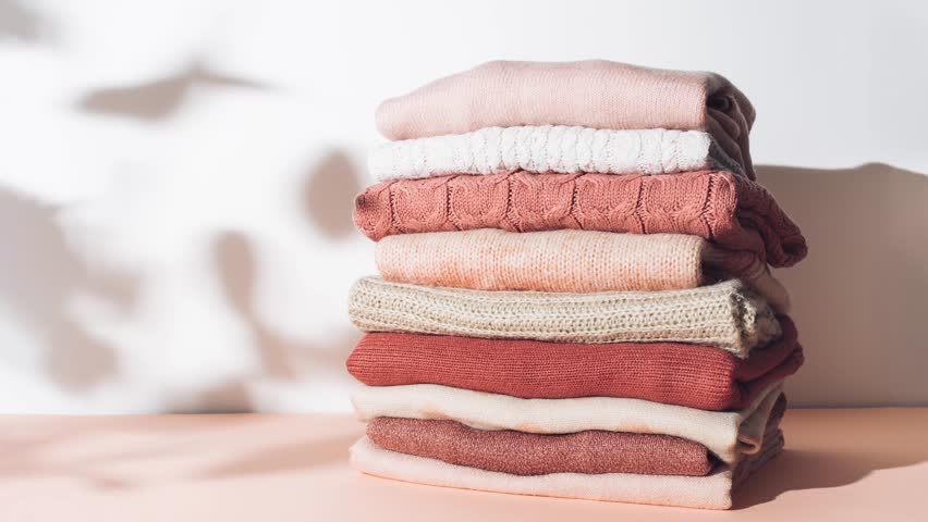 Creative stop motion animation made with pile of textured woolen sweaters in pastel colors against sunlit white background. Autumn and winter fashion aesthetic. Royalty-Free Stock Footage #1099666465