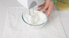 A man beats egg white with a mixer in a transparent bowl in the kitchen. Several spoons of sugar. High quality 4k footage
