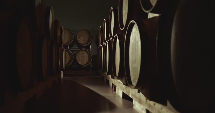 Aged wooden barrels with a wine , brandy or whiskey in a big warehouse . Dolly , gimbal movement a long row of wine barrels at a vintage winery with alcohol . Wine preparation and fermenting process Royalty-Free Stock Footage #1099674519