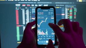 Crypto investor using mobile phone app for buying cryptocurrency in front of stock market financial screen, close up. Trader investor holding mobile phone analyzing financial crypto stock market price - Powered by Shutterstock - Get 15% off with code: PIKWIZARD15