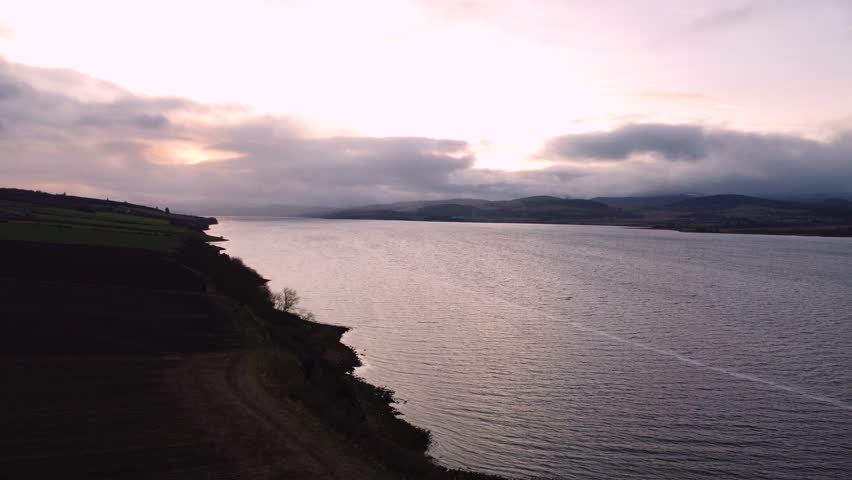 A short flight over the shore and ocean with mountains and hills in the distance across the water. The shot is in 4k and was taken with a drone