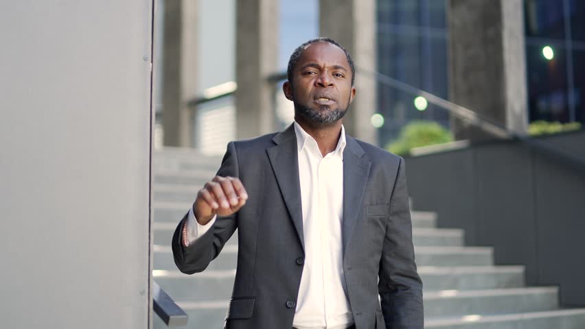 Sick african american mature man suffering from heart pain standing outside in front of office building. A middle-aged businessman in a formal suit holds his hand to his chest. He has a heart attack Royalty-Free Stock Footage #1099682499