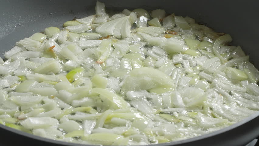 Close-up of finely chopped white onion are being fried with a wooden spoon in vegetable oil in a non-stick frying pan