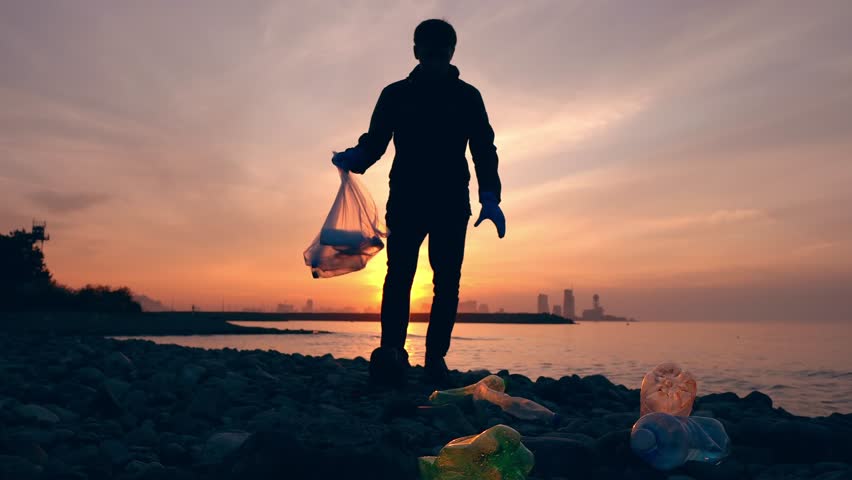Process of cleaning stone beach from plastic waste. Man picks up plastic bottles in trash bag. Environmental pollution concept | Shutterstock HD Video #1099685719