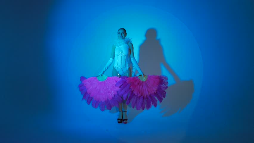 Brunette in a white dance bodysuit with a bright evening make-up with a white boa with large fans with colored red and blue lighting