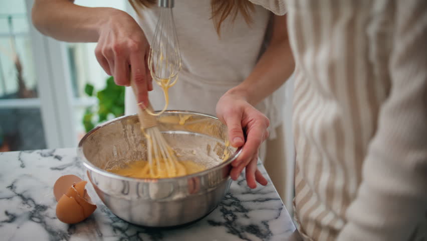 Mom daughter kneading dough in bowl indoors close up. Laughing woman mixing ingredients at kitchen. Adorable child helping lady. Mother kid cooking together at home interior. Family traditions concept | Shutterstock HD Video #1099687651