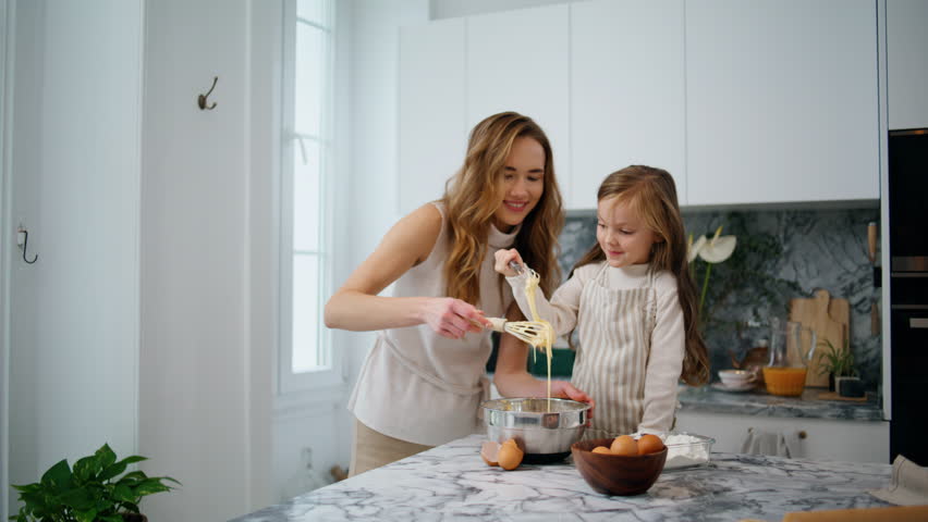 Cheerful family making dough at home. Smiling mother having fun with child at kitchen interior. Adorable preschooler girl doing bakery helping millennial mom. Homemade food and little helper concept