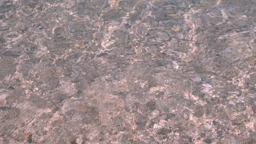 Clear sea on white warm pebbles. A beautiful view of white small pebbles under the warm sea water on the shore. A concept of summer sea traveling under sun. | Shutterstock HD Video #1099688139