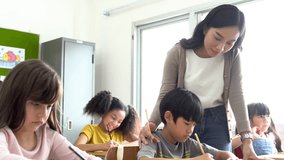 Asian school teacher assisting students in classroom. Young woman working in school helping boy with his writing, education, support, care. - Powered by Shutterstock - Get 15% off with code: PIKWIZARD15