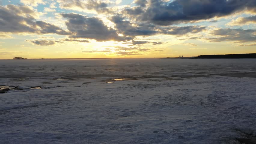 Aerial video view of flying over ice of frozen Ob sea at amazing sunset with yellow Sun and red clouds.
