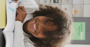 Vertical video portrait of smiling african american schoolboy sitting at desk in class, copy space. Education, childhood, inclusivity, school and learning concept.