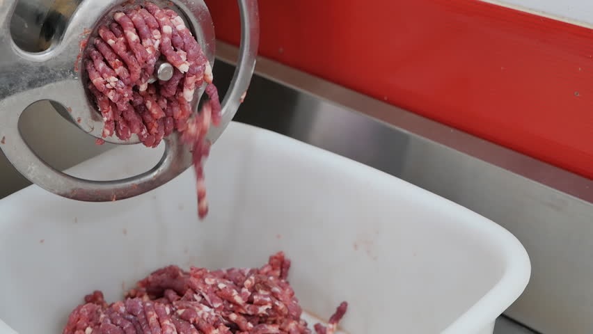 The process of twisting meat into minced meat using an electric meat grinder in a grocery store. Close-up of medium-fat ground beef falling into a white plastic container. | Shutterstock HD Video #1099692837