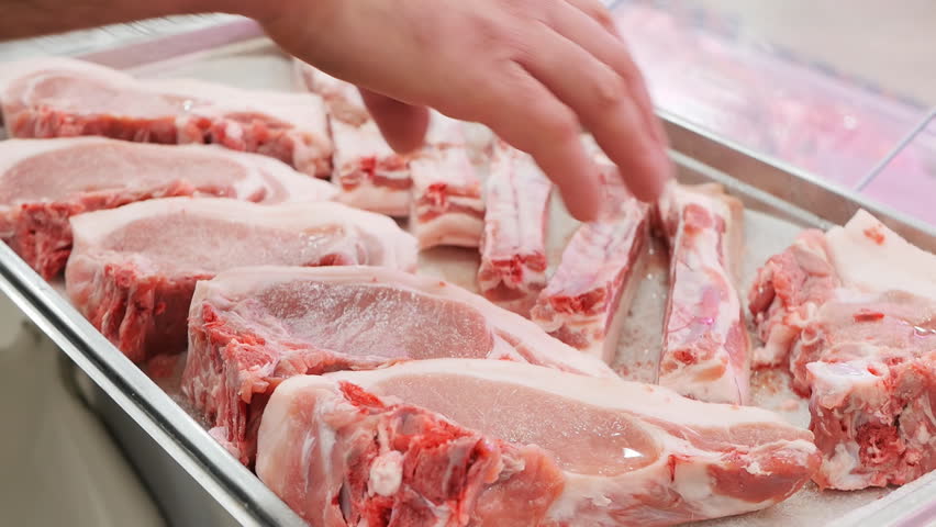 The hands of the butcher take pieces of cut fresh meat lying on a tray with a polystyrene bedding. retail trade in meat products in grocery stores of large supermarkets. Food industry. | Shutterstock HD Video #1099692857