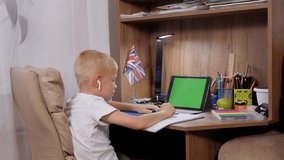 A small schoolboy boy is engaged with a teacher online, distance learning. The child is sitting at his desk in front of a tablet with a green screen. - Powered by Shutterstock - Get 15% off with code: PIKWIZARD15