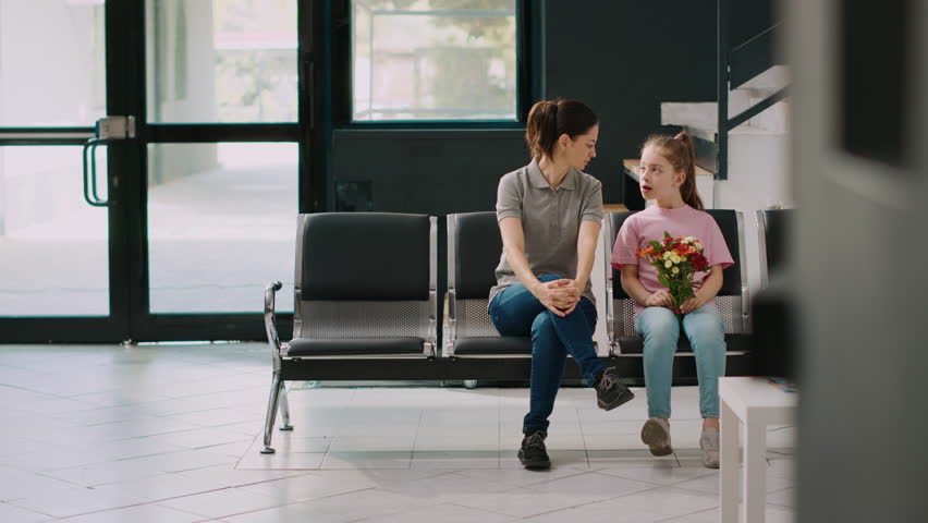 Elderly patient in wheelchair meeting with family in hospital waiting room, talking to woman and little girl in lobby. Senior person with disability receiving medical assistance at health center. | Shutterstock HD Video #1099702871