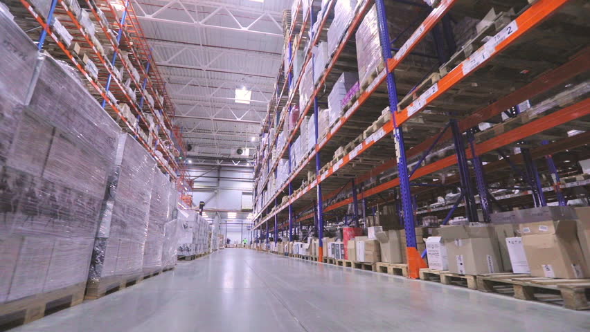 The worker walks through the warehouse. A worker is carrying a rokla through a large warehouse. Digitalization of production. Futuristic production concept. Royalty-Free Stock Footage #1099704011