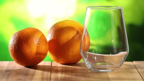 orange juice is poured into a glass. oranges on the table in the summer sun. fresh fruits on a green background. High quality 4k footage