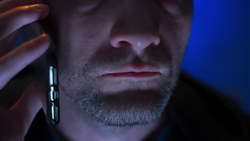anonymous phone call. man mobile phone talk. speaking mouth closeup. man talking on smartphone, lower face close up. one caucasian person in a dark talking on phone, low light, neon blue background Royalty-Free Stock Footage #1099707901
