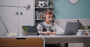 Little cute boy in headphones having a video call talking using laptop sitting in the living room. Online learning, distance learning, learning at home.